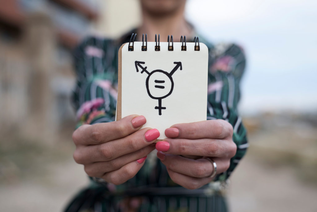 LGBTQ New Year's Resolution. Closeup of a young Caucasian woman outdoors showing a notepad in front of her with a transgender symbol drawn in it