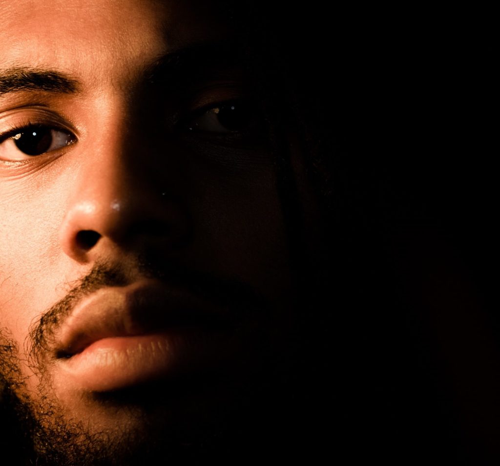 A close up of a black man's face with half covered in darkness.